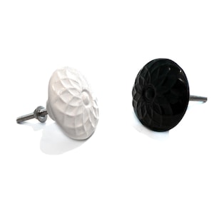 Könnte beinhalten: Zwei Keramik-Schrankknöpfe mit Blumenmuster. Ein Knopf ist weiß und der andere ist schwarz.