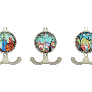 以下が含まれることがあります： 3つの装飾的な金属製の壁掛けフックのセット。各フックは、気まぐれな街のシーンの丸くカラフルなイラストが特徴です。フックはシルバー仕上げで、コートやアクセサリーを掛けるのに最適なダブルフックデザインです。