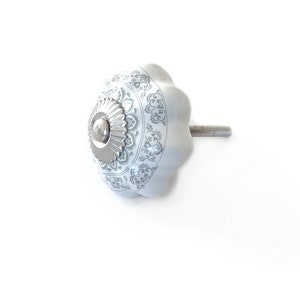 Peut inclure: Bouton de porte en céramique blanche avec une base en métal argenté et un motif floral gris.