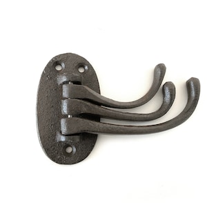 Könnte beinhalten: Ein dunkelbrauner Kleiderhaken aus Gusseisen mit drei gebogenen Haken. Der Haken ist auf einer ovalen Grundplatte mit drei Schraubenlöchern oben und einem unten montiert. Die Haken sind angelenkt.