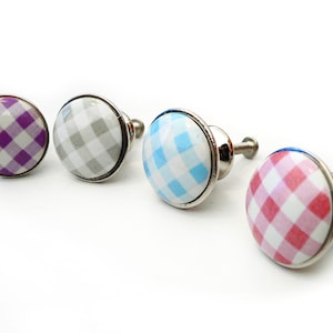 May include: Four ceramic cabinet knobs with a silver base. The knobs feature a white background with a checkered pattern in purple, grey, blue, and pink.