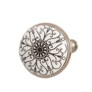 Könnte beinhalten: Weißer Keramik-Schrankknopf mit einem schwarz-weißen Blumendesign. Der Knopf hat eine silberne Oberfläche.