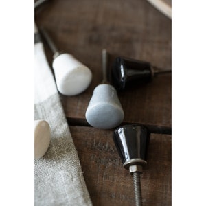 Könnte beinhalten: Sortiment an Keramik-Schrankknöpfen in Weiß, Grau und Schwarz. Die Knöpfe haben eine abgerundete, glockenförmige Form.