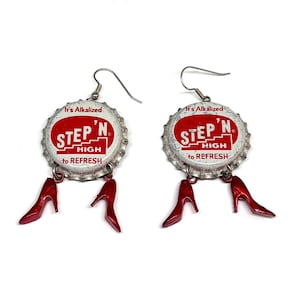 Könnte beinhalten: Ein Paar handgefertigte Ohrringe mit Flaschendeckeln mit dem Text "STEP 'N HIGH to REFRESH" in Rot und Weiß. Jeder Ohrring hat einen kleinen, roten High-Heel-Schuh-Anhänger, der darunter hängt, mit silberfarbenen Ohrhaken.