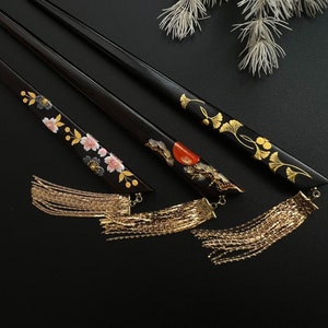 May include: Three black hair sticks with gold tassels. Each stick has a different floral design painted on it in gold, red, and pink.