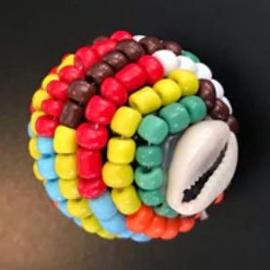 May include: Multicolored beaded ball with a white cowrie shell accent. The ball is made of small, round beads in shades of red, orange, yellow, green, blue, brown, and white.