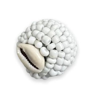 May include: White beaded ball with a cowrie shell accent. The ball is made of small, white beads that are tightly packed together. The cowrie shell is a natural shell that is often used in jewelry and crafts.