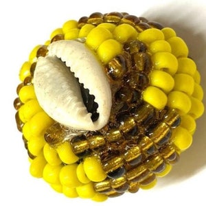 May include: A round bead made of yellow and brown beads with a white cowrie shell in the center.