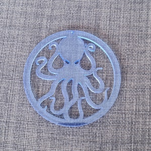 Könnte beinhalten: Ein blauer Acryl-Anhänger in Kreisform mit einem Ausschnitt eines Kraken in der Mitte.