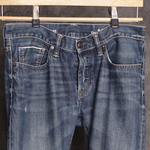 Puede incluir: Un par de pantalones vaqueros azules de mezclilla con corte recto. Los pantalones tienen cierre de botón y cinco bolsillos.