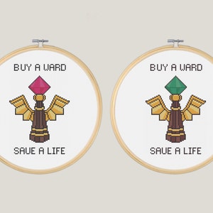 May include: Two embroidery hoops with the text "Buy a Ward Save a Life" and a pixelated image of a ward from the video game League of Legends. One ward has a pink gem and the other has a green gem.
