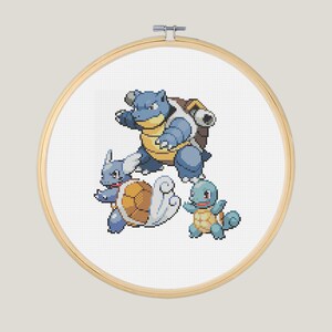 May include: A cross-stitch embroidery hoop with a white background and three blue and yellow Pokemon characters: Blastoise, Wartortle, and Squirtle.