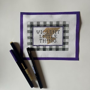 May include: A purple-bordered canvas with a black and white checkered pattern. The canvas features the text "VIOLENT LITTLE THING" in gold lettering with a lightning bolt graphic.