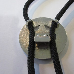 Puede incluir: Un bolo tie plateado con un dise&ntilde;o de estrella de cinco puntas. La corbata est&aacute; hecha de cord&oacute;n trenzado negro y tiene puntas plateadas.