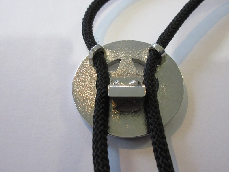 Puede incluir: Un bolo tie plateado con un dise&ntilde;o de estrella de cinco puntas. La corbata est&aacute; hecha de cord&oacute;n trenzado negro y tiene puntas plateadas.