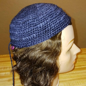 May include: A blue crocheted beanie with a textured pattern. The beanie is on a mannequin head with brown hair.