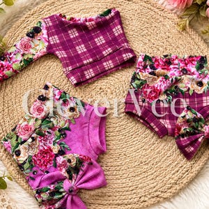 Könnte beinhalten: Ein langärmeliges Oberteil, zwei Shorts und eine Haarschleife mit einem magentafarbenen und weißen Karomuster in Kombination mit einem lebendigen Blumenmuster aus rosa Rosen und grünen Blättern. Der Text Clever Vee ist mittig aufgedruckt.