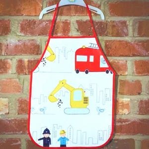 Può includere: Grembiule per bambini rosso e bianco con una scena di città con un escavatore giallo, un camion dei pompieri rosso e due operai edili.
