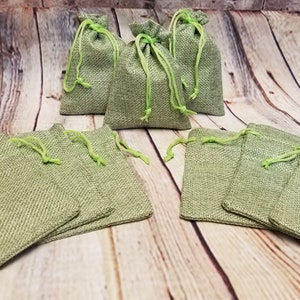 May include: Ten small green burlap drawstring bags with green drawstrings. The bags are arranged in two rows on a wooden surface.