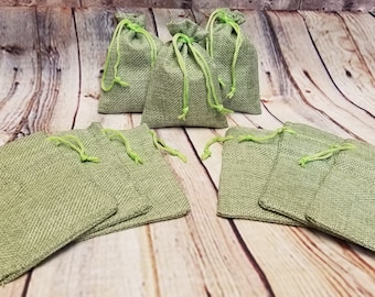 May include: Ten small green burlap drawstring bags with green drawstrings. The bags are arranged in two rows on a wooden surface.