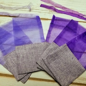 May include: Purple organza gift bags with a gray burlap bottom. The bags are folded and stacked on a light wood surface.