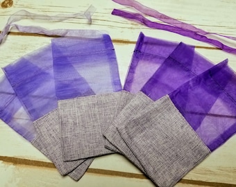 May include: Purple organza gift bags with a gray burlap bottom. The bags are folded and stacked on a light wood surface.