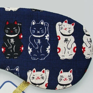 May include: Blue fabric eye mask with a repeating pattern of white and black lucky cat figures. The cats are in a sitting position with their paws raised. The text "lucky" is written on each cat in Japanese characters.