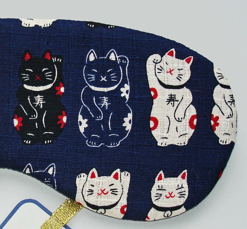 May include: Blue fabric eye mask with a repeating pattern of white and black lucky cat figures. The cats are in a sitting position with their paws raised. The text "lucky" is written on each cat in Japanese characters.