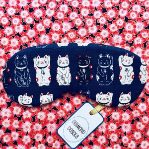 May include: A blue sleep mask with a pattern of white and black Japanese Maneki-Neko (beckoning cat) figures. The mask has the text "Diamond Desola" on a white tag.