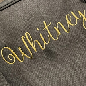 May include: A dark grey fabric bag with the name "Whitney" embroidered in gold thread.