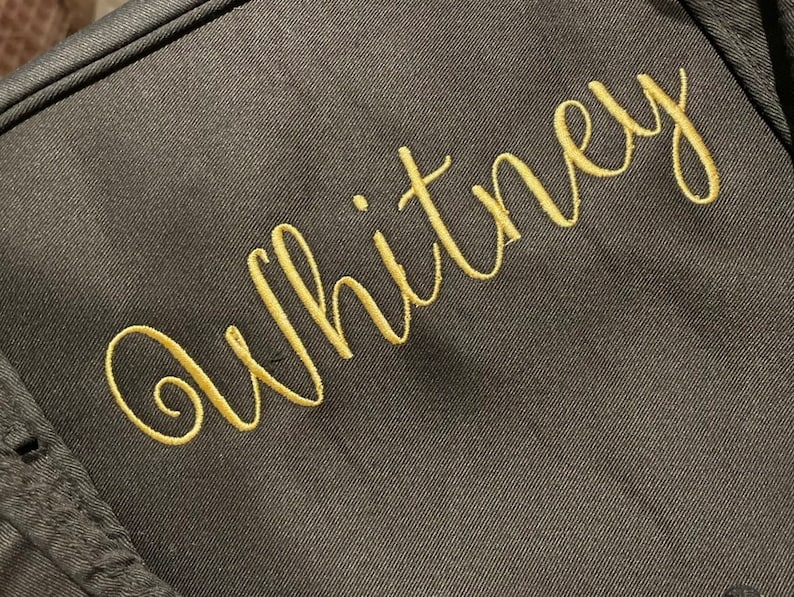 May include: A dark grey fabric bag with the name "Whitney" embroidered in gold thread.