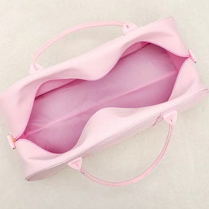 May include: A light pink duffel bag with two handles. The bag is open and the inside is visible.