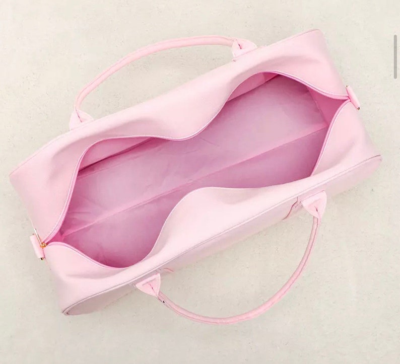 May include: A light pink duffel bag with two handles. The bag is open and the inside is visible.