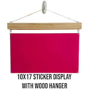 May include: A 10x17 inch pink sticker display with a wooden hanger. The hanger is attached to the top of the display with string.