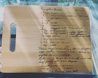 May include: A handwritten pumpkin bread recipe on a wooden cutting board. The recipe includes ingredients like sugar, margarine, pumpkin, eggs, water, raisins, nuts, baking powder, baking soda, flour, cinnamon, ground cloves, and salt. The recipe also includes instructions for creaming the sugar and shortening, blending in the dry ingredients, and baking the bread in a loaf pan at 350 degrees Fahrenheit. The recipe notes that small loaves bake for 45 minutes and large loaves bake for 1 hour.