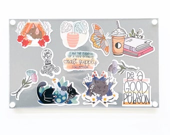 May include: A set of colorful stickers featuring a variety of designs, including a cat, a butterfly, a potted plant, a cup of coffee, a stack of books, a lightbulb with tentacles, a cat with a potion, a cat with flowers, and a sticker that says "Be a Good Person".