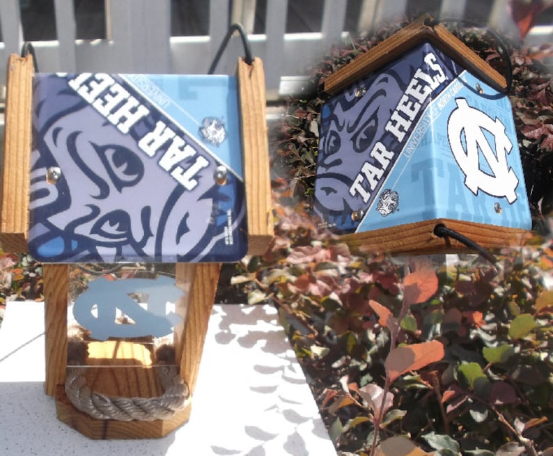 May include: Wooden birdhouse featuring the University of North Carolina Tar Heels logo and colors. The birdhouse has a light blue roof with the words "TAR HEELS" and the UNC logo. The front has a clear panel with the UNC logo and a rope perch.
