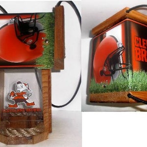 Może przedstawiać: Drewniana karmnik dla ptak&oacute;w w stylu Cleveland Browns. Karmnik ma przezroczyste plastikowe okno z kresk&oacute;wkowym obrazkiem gracza Browns. Karmnik jest ozdobiony logo i kolorami drużyny.