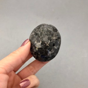May include: A smooth, oval-shaped, dark gray gemstone with iridescent flecks.