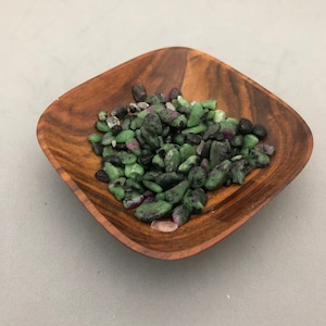 May include: A small wooden bowl filled with green, black, and pink tumbled stones.