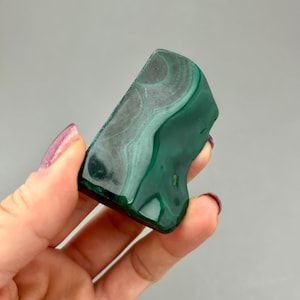 May include: A green malachite stone with white veining. The stone is smooth and polished, and has an irregular shape.