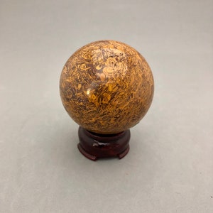 May include: A brown and gold sphere with a swirling pattern sits on a dark wood stand.
