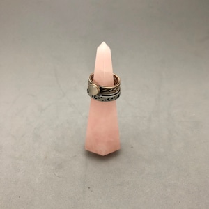 May include: A pink rose quartz crystal point ring holder. The crystal is shaped like a pyramid and has a smooth, polished surface.