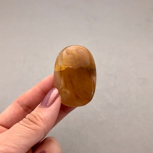 May include: A smooth, polished, oval-shaped, light brown and white agate gemstone.