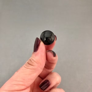 May include: A black, round, smooth, polished stone held in a hand with dark red nail polish.