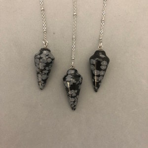 May include: Three black and white snowflake obsidian crystal pendulums with silver chains.