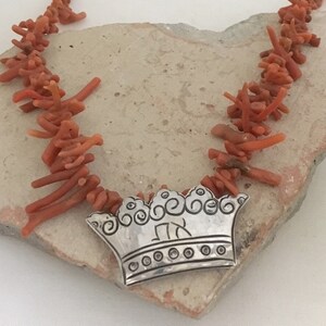 May include: A silver crown pendant with an engraved initial "R" hangs from a necklace made of orange coral branches.