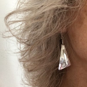 May include: Silver earrings with a hammered finish and a music note design.