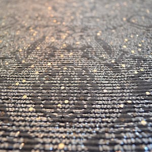 May include: Close-up of a black fabric with a silver and gold shimmery pattern. The fabric has a textured, woven look.