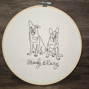 Op de afbeelding: Borduurwerk op een hoepel met twee honden, Brody en Roxy, in een eenvoudige lijntekening stijl.